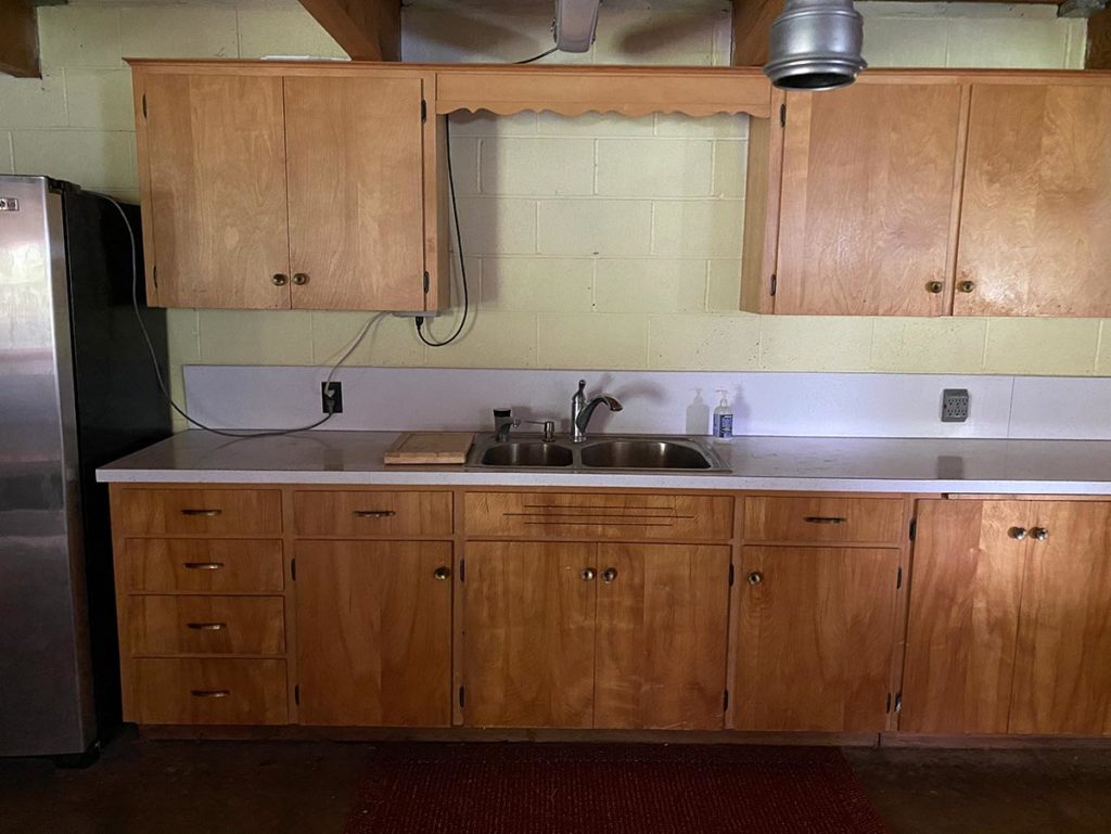 A stainless steel sink and old, wood cabinetry with weak yellow painted brick