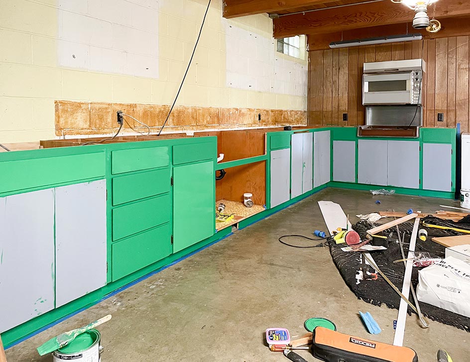 Partially primed and painted green cabinets in an old basement kitchen