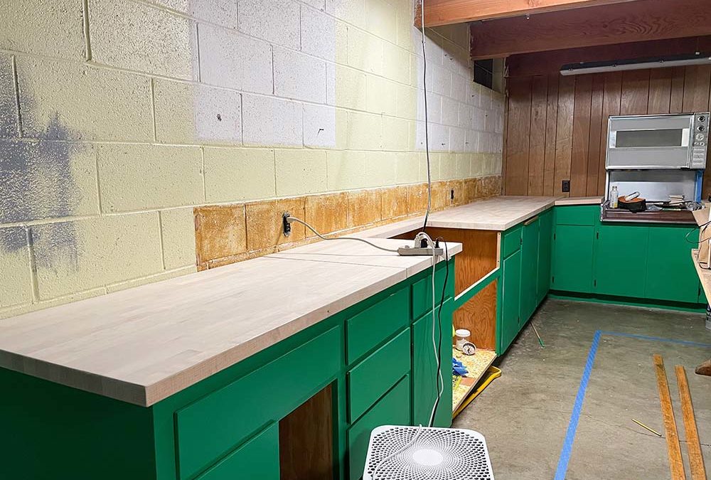 Butcher block countertops on green cabinetry in a basement kitchen