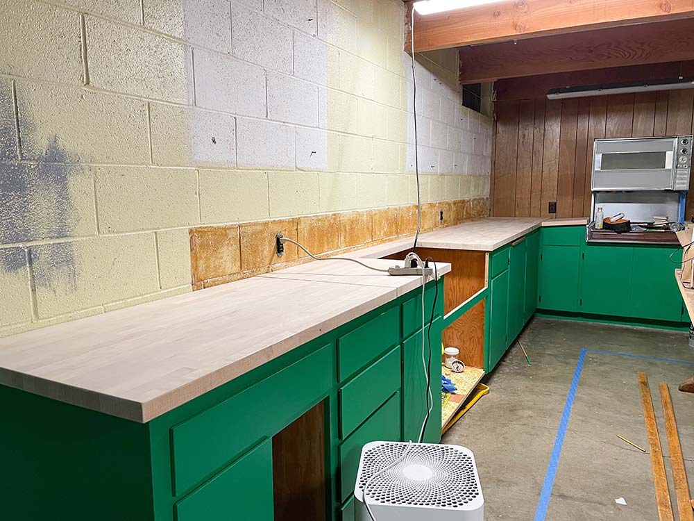 Butcher block countertops on green cabinetry in a basement kitchen