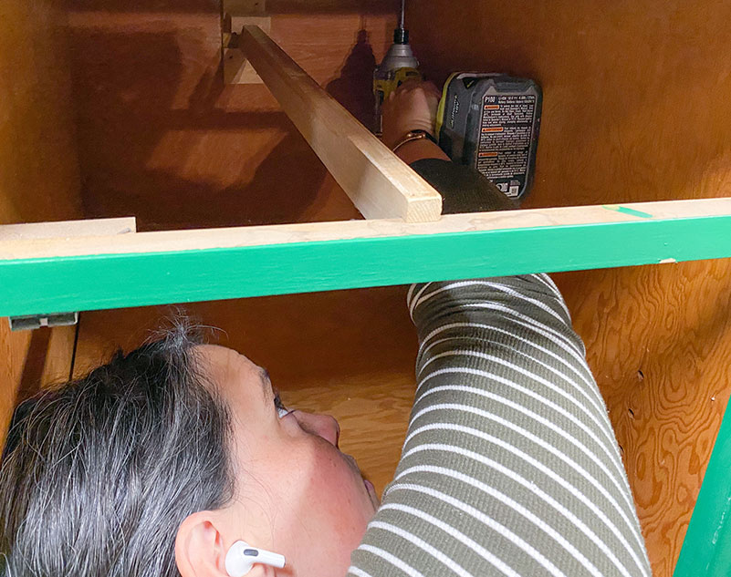 Racheal Jackson crawling into cabinetry to secure them to the butcher block countertops